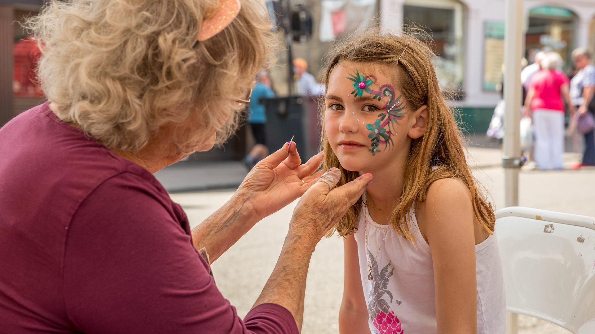 Older lady wearing a pink top facepainting a young girl