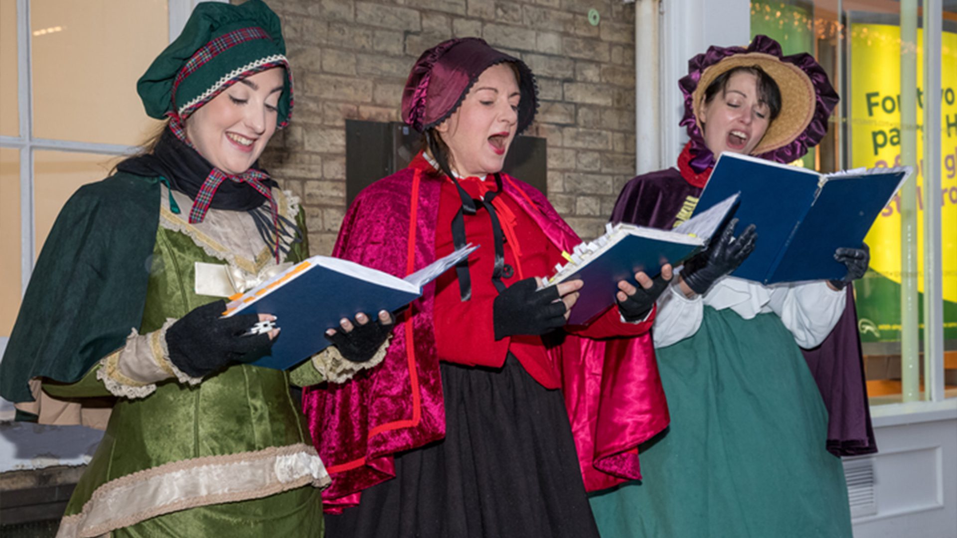 Three carol singers sing joyfully with their hymn books
